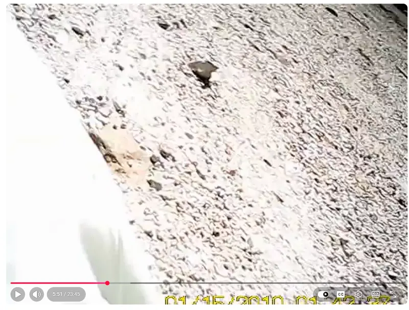 Frame from Jeffrey Weinhaus’s watch camera showing a dark holster shaped object lying on the gravel near him after the shooting, with the muzzle end pointed away from the camera. Frame from Jeffrey Weinhaus’s watch camera showing a dark holster shaped object lying on the gravel near him after the shooting, with the muzzle end pointed away from the camera.
